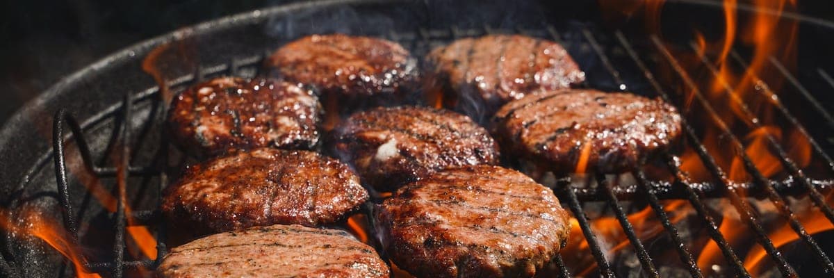 Close-up van hamburgers die op een gloeiende grill liggen te bakken.